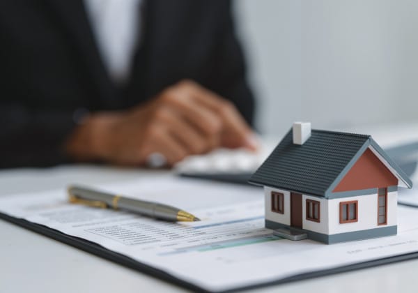 Vertrag für Immobilienverkauf in Berlin liegt auf einem Tisch, darauf steht ein Modell eines Hauses