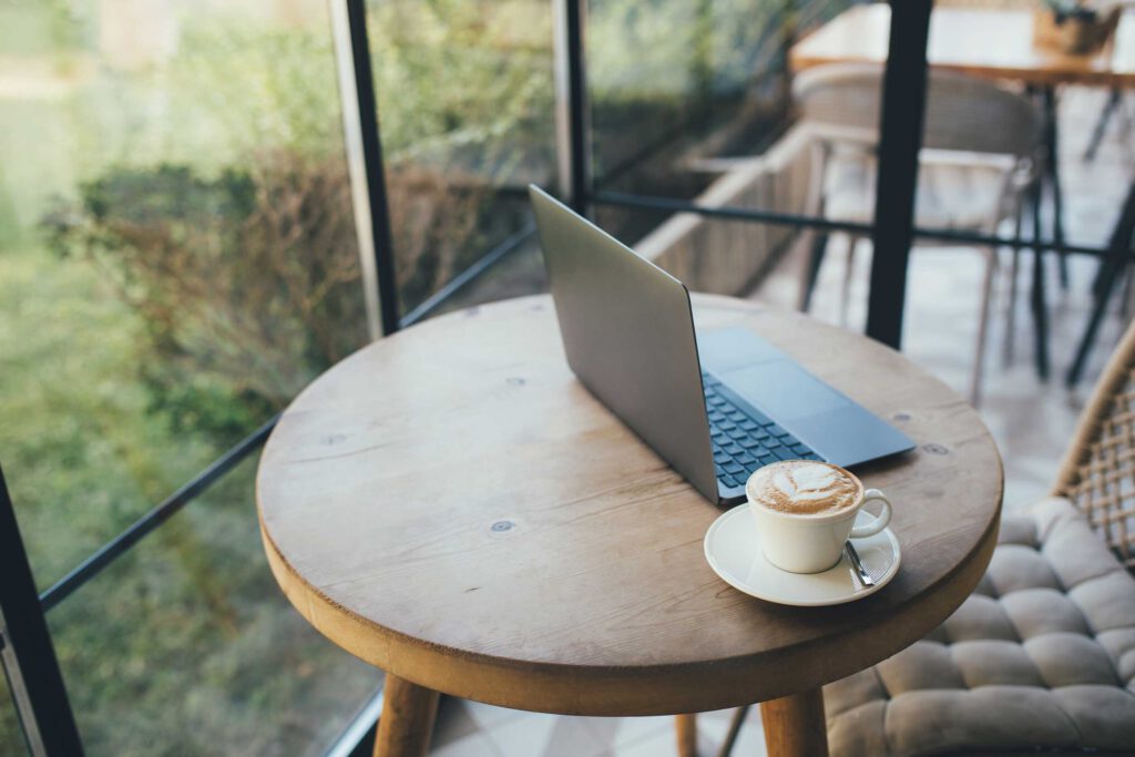 Schöner runder Holztisch mit passendem Stuhl am Fenster mit Laptop und Cappuccino.